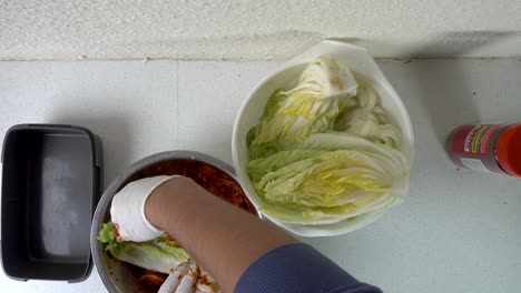 Männliche-Hände,-Die-Chilipaste-Auf-Kohl-Für-Kimchi-Auftragen-Und-Es-Wegpacken