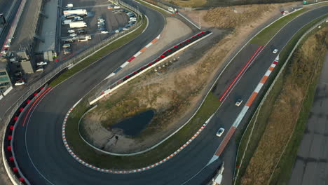 F1-Racing-Cars-Moving-On-A-Sharp-Turn-On-The-Circuit-Of-Zandvoort,-The-Netherlands---aerial-drone-shot