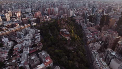 High-aerial-view-flying-over-Santa-Lucia-hill-surrounded-by-vast-high-rise-urban-cityscape