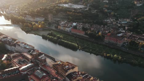 Golden-hour-sunlight-shining-on-calm-Arno-River-at-Florence,-dawn,-aerial