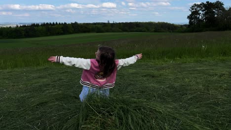 A-young-little-girl-playing-and-falls-on-her-back-onto-a-pile-of-mowed-grass-in-a-field