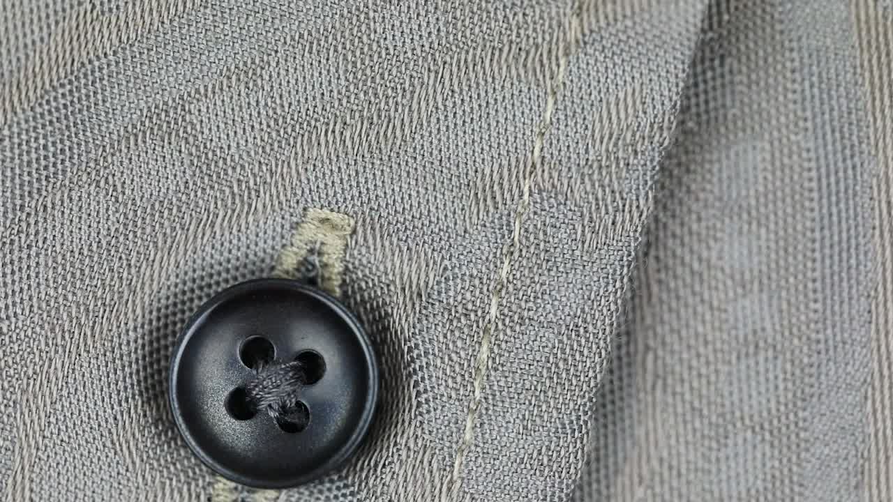 Premium stock video - Black button with four holes fastened on wool fabric