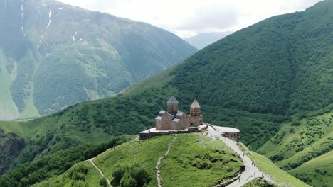 Ancient-Gergeti-Trinity-Church-in-majestic-mountain-landscape,-distance-aerial-orbit-view
