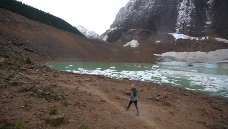 Lonely-Woman-Walking-by-Glacial-Lake-With-Icebergs-Under-Glacier-in-Canadian-Highlands