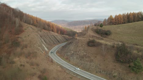 An-aerial-drone-view-of-cars-driving-on-a-winding-road-running-through-a-canyon-in-late-autumn