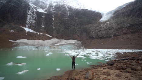 Back-View,-Young-Woman-Raising-Arms-in-Front-of-Scenic-Glacial-Lake-and-Glacier