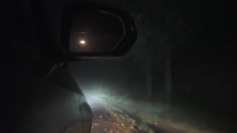 Car-driving-at-night,-side-low-front-view-of-mirror-and-countryside-road-lost-in-fog