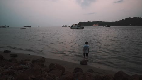 An-excited-young-boy-jumping-up-and-down-having-fun-playing-in-the-shallow-waters-along-the-bank-of-the-Mahadayi-River-at-sunset,-Goa,-India