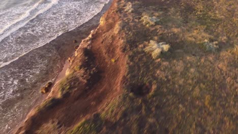 Spectacular-fpv-flight-over-edge-of-giant-lighting-cliffs-during-sunset---Ocean-waves-reaching-sandy-beach---Mar-del-Plata,Argentina