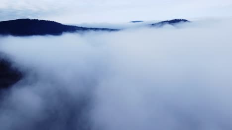 Moody-aerial-mountain-forest-in-clouds-revealing-peaks