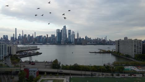 Aerial-drone-view-approaching-the-Hudson-yards-district,-from-Jersey-city---birds-in-frame