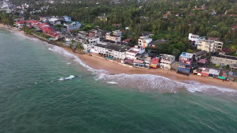 Drone-flying-over-ocean,-beach-and-waves-in-popular-surfing-destination-of-Hikkaduwa-in-the-south-coast-of-Sri-Lanka