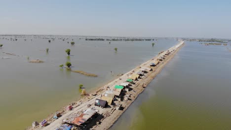 Aerial-View-Over-Elevated-Strip-Of-Land-Housing-Makeshift-Tents-Of-Surrounded-By-Flooded-Landscape-In-Mehar