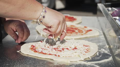 Lady's-hands-spreading-mozzarella-cheese-on-raw-pizza-dough-outdoors