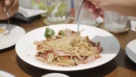 Vista-De-Cerca-A-Mano-Usando-Tenedor-Para-Comer-Espaguetis-Picantes-Con-Salchicha-En-Plato-Blanco