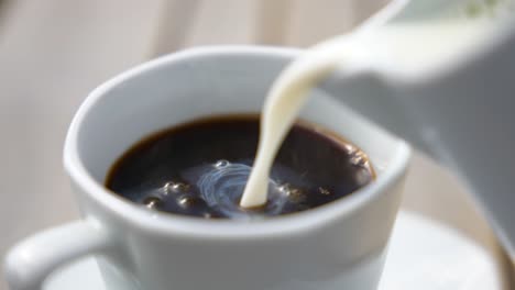 Close-up-Of-Fresh-Milk-Pouring-Into-Hot-Black-Coffee-In-A-White-Ceramic-Cup
