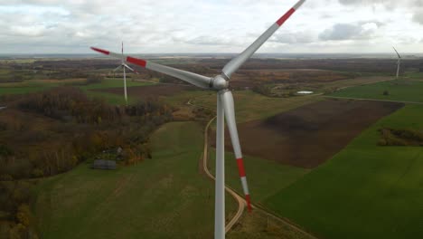 Luftaufnahme-Von-Mehreren-Sich-Drehenden-Windturbinen-Zur-Erzeugung-Erneuerbarer-Energie-In-Einem-Weiten-Ländlichen-Gebiet-An-Einem-Bewölkten-Tag-In-4k