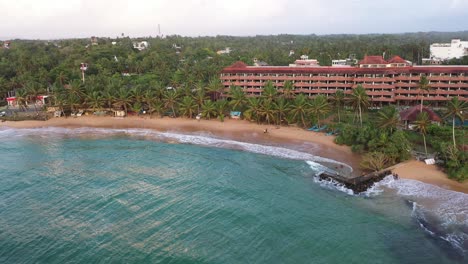 Aerial-descending-over-ocean,-beach-and-waves-in-popular-surfing-destination-of-Hikkaduwa-in-the-south-coast-of-Sri-Lanka