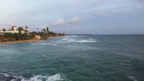Aerial-flying-at-low-altitude-fast-above-ocean-and-waves-in-popular-surfing-destination-of-Hikkaduwa,-Sri-Lanka