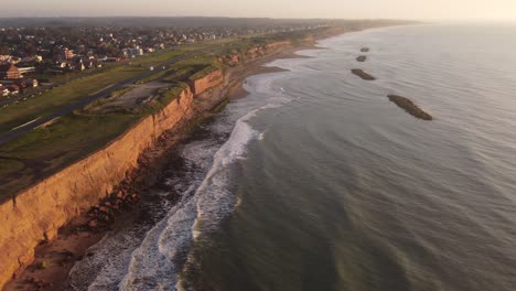 Panorama-aerial-shot-of-lighting-rocky-cliffs-and-crashing-waves-from-Atlantic-Ocean-during-sunset---Golden-sunset-time-at-horizon-in-suburb-area-of-South-America