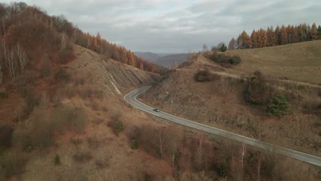 An-aerial-drone-view-of-a-car-driving-on-a-winding-road-running-through-a-canyon-in-late-autumn