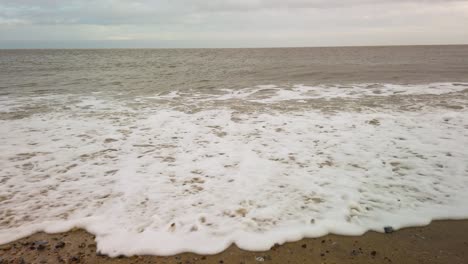 Sea-wave-at-sandy-beach-in-north-sea,-Great-Yarmouth,-Norfolk,-England---handheld-shot
