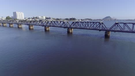 Flying-towards-Matapihi-Railway-bridge-with-Tauranga-city-in-background,-Bay-of-Plenty,-aerial