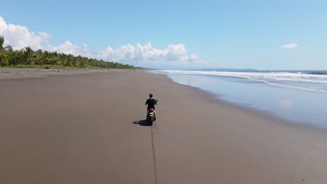 Young-man-on-scooter-riding-over-the-hard-sand-of-a-wide,-long-tropical-beach
