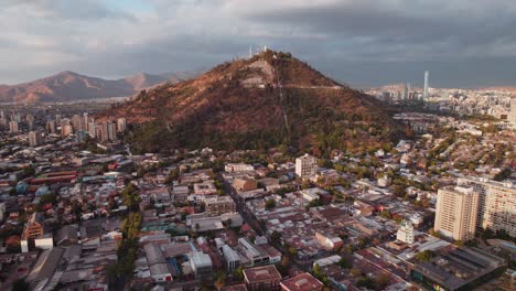 Sunset-aerial-view-towards-glowing-vast-cityscape-surrounding-Cerro-San-Cristobal-mount