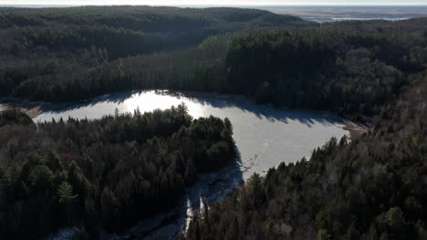 Aerial-view-of-snowy-lake-and-forest-during-late-winter---drone-shot