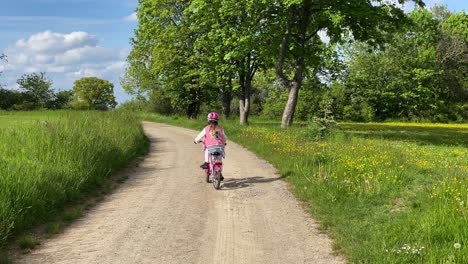 A-young-girl-riding-her-cycle-on-a-dusty-road-through-a-meadow