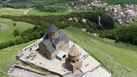 Cinematic-fly-over-Gergeti-Trinity-Church-revealing-small-town-near-hill-slope