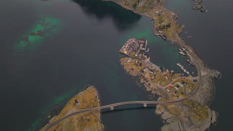 Top-down-aerial-view-above-winding-Reine-bridge-leading-to-Lofoten-harsh-frozen-mountain-landscape