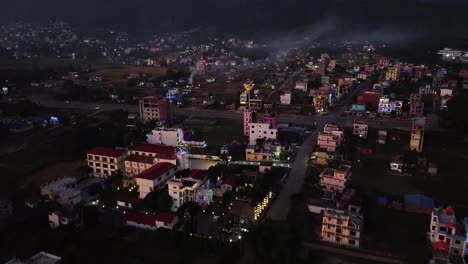 A-low-level-aerial-over-the-city-of-Surkhet,-Nepal-in-the-late-evening-capturing-the-city-lights-with-the-mountain-in-the-background