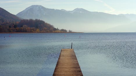 Jetty-pier-on-Tegernsee-in-autumn-with-snow-capped-mountains-of-the-alps-in-the-background