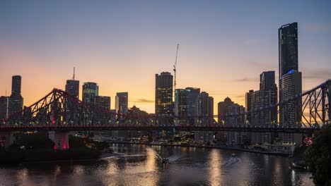Day-to-night-time-lapse-of-iconic-story-bridge-with-beautiful-radiance-sky-and-downtown-cityscape-in-the-background,-ferries-cruising-across-the-river,-Brisbane-city,-Queensland