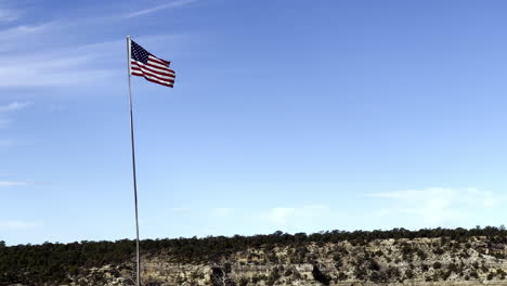 Ein-Mittlerer-Schuss-Einer-Flagge-Der-Vereinigten-Staaten-Von-Amerika,-Die-Im-Wind-Mit-Blick-Auf-Den-Grand-Canyon-Folgt