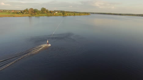 Aerial-view-showing-drone-pulling-wakeboarder-cruising-over-sea-during-beautiful-sunset-time