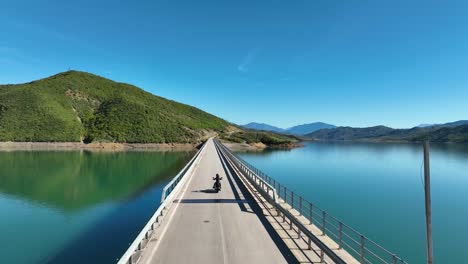 Motorcycle-riding-over-a-bridge-crossing-a-blue-lake
