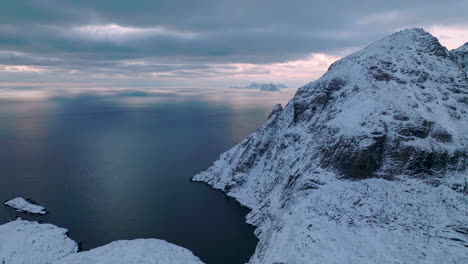 Hohe-Schneebedeckte-Berggipfel-Der-Lofoten-Inseln-Luftbild,-Das-Sich-über-Dem-Idyllischen-Blauen-Ozean-Erhebt