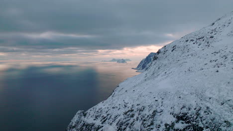 Snow-covered-Lofoten-islands-mountain-slope-aerial-view-overlooking-blue-ocean-seascape