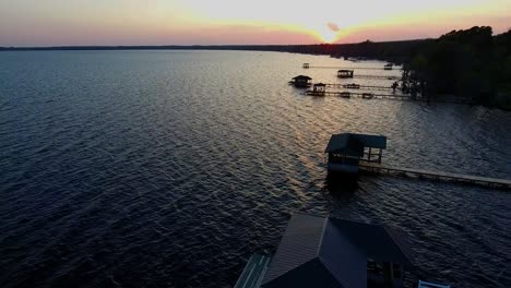 Luftaufnahme-Des-Sonnenuntergangs-Auf-Einem-Unberührten-See,-Während-Die-Kamera-Von-Sonnenbeschienenen-Docks-In-Blaues-Wasser-Kippt