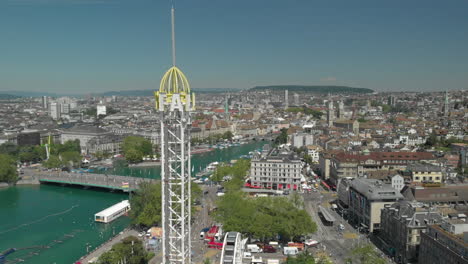 Aerial-drone-shot-slow-orbiting-flyby-around-amusement-park-free-fall-tower-with-the-city-and-lake-of-Zürich,-Switzerland-in-the-background-during-Zürichfest