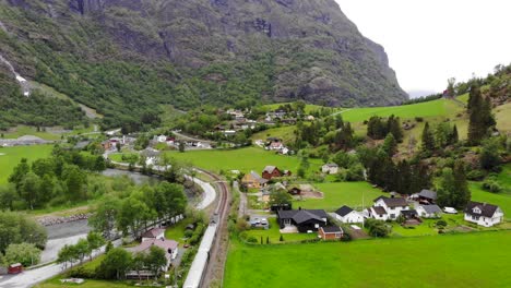 Aerial:-Flåm-train-going-through-a-valley-among-green-meadows-and-by-a-river