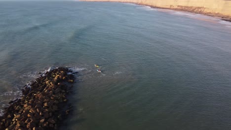 Kayak-Team-rowing-in-wide-Atlantic-Ocean-against-breakwater-waves-during-sunset---Aerial-orbiting-shot
