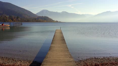 Long-jetty-pier-in-placid-lake-with-background-mountains-in-autumn