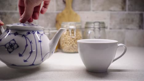 Gießen-Sie-Eine-Tasse-Tee-Mit-Zwei-Händen-Mit-Lebensmittelzutaten-Im-Hintergrund