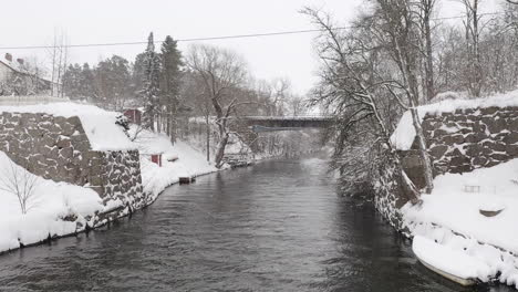 Drone-shot-of-a-small-concrete-bridge-over-a-river-stream-on-a-snowy-winter-day-in-Sweden