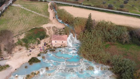 In-Saturnia-Italy,-the-drone-rises-up-while-tilting-down-revealing-the-entire-hot-spring-baths