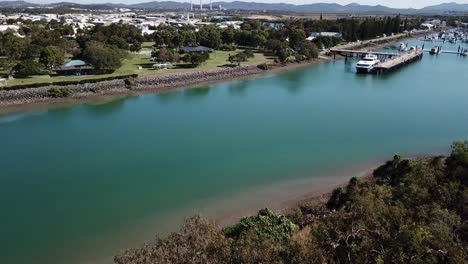 Drone-aerial-pan-up-over-park-and-blue-water-harbour-on-a-sunny-day